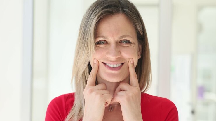 A woman smiling and pointing at her dimples
