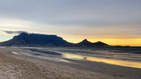 Atemberaubende-Kapstadt-Tafelberg-Strandlandschaft,-Goldgelb-orangefarbener-Sonnenuntergang,-Südafrika,-Möwenvogel,-Der-Wegfliegt,-Ebbe,-Unglaubliche-Küstenlinie,-Zeitlupe,-Schwenk-Nach-Links