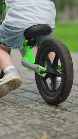 a woman with painted nails supports her young son who is learning how to ride a bicycle, the boy uses his leg for balance as she lets him move forward independently