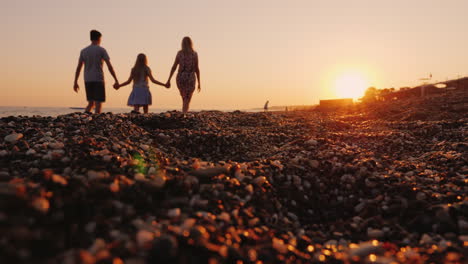 Young-Family-With-A-Niño-Walking-Along-The-Beach-At-Sunset-In-The-Foreground-A-Pebble-Beach
