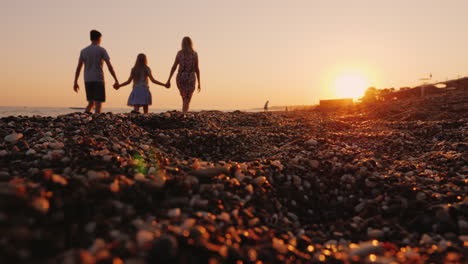 Junge-Familie-Mit-Einem-Kind,-Das-Bei-Sonnenuntergang-Am-Strand-Entlang-Spaziert,-Im-Vordergrund-Ein-Kiesstrand