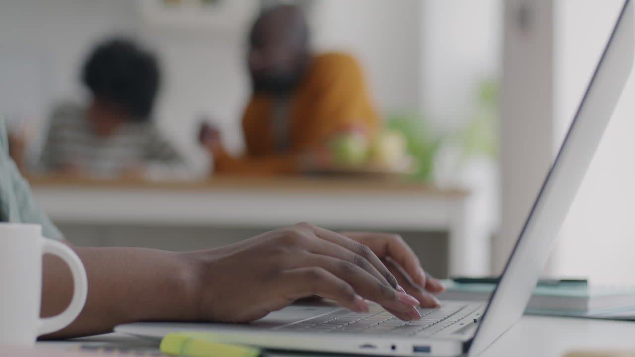 Woman Working on Laptop at Home with Family in Background