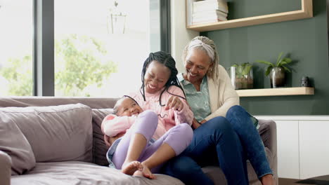 happy african american mother,daughter and grandmother embracing on couch and laughing, slow motion
