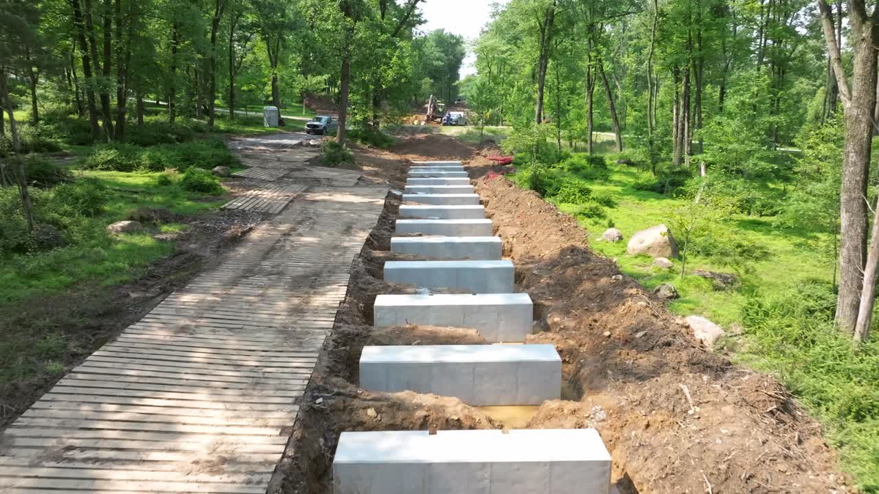 Workers are constructing a New Rail Road Trestle in a lush forest. They place large stone slabs into the ground while maintaining the natural surroundings. Heavy machinery