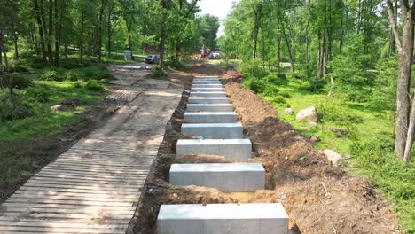 workers are constructing a new rail road trestle in a lush forest. they place large stone slabs into the ground while maintaining the natural surroundings. heavy machinery