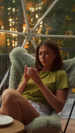 balanced woman sits comfortably holding cup of coffee in hands. young woman alone looks with thoughtful deep look without changing emotions