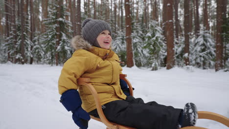 portrait of a smiling boy 3-4 years old in slow motion who rides a sled in a snowy forest in winter