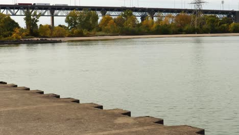 Trucks-and-cars-travel-across-an-elevated-bridge,-beyond-a-calm-expanse-of-water