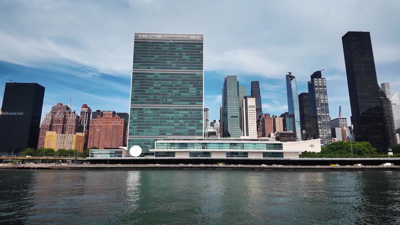 Vista panorâmica à beira-rio da Sede das Nações Unidas com o horizonte de Midtown Manhattan, o Edifício Chrysler e o East River sob céus azuis dramáticos em Nova York.