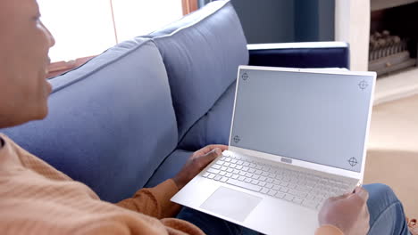 feliz hombre afroamericano sentado en el sofá usando una computadora portátil con espacio de copia en casa, cámara lenta