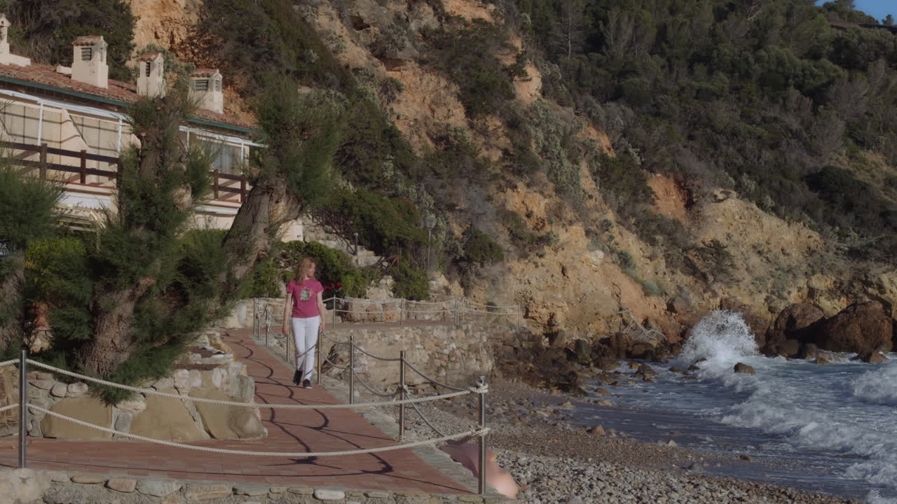 una chica camina desde una casa de playa de lujo italiana por un camino pintoresco, observa las olas del océano