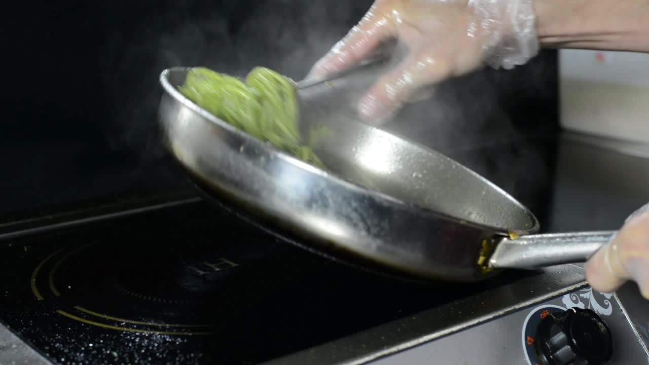 전기 스토브에서 녹색 스파게티 파스타를 요리하는 주방의 요리사