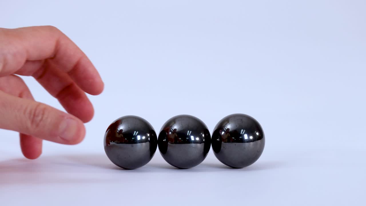 Hands reach into frame to collect three metallic magnetic balls against a plain white background