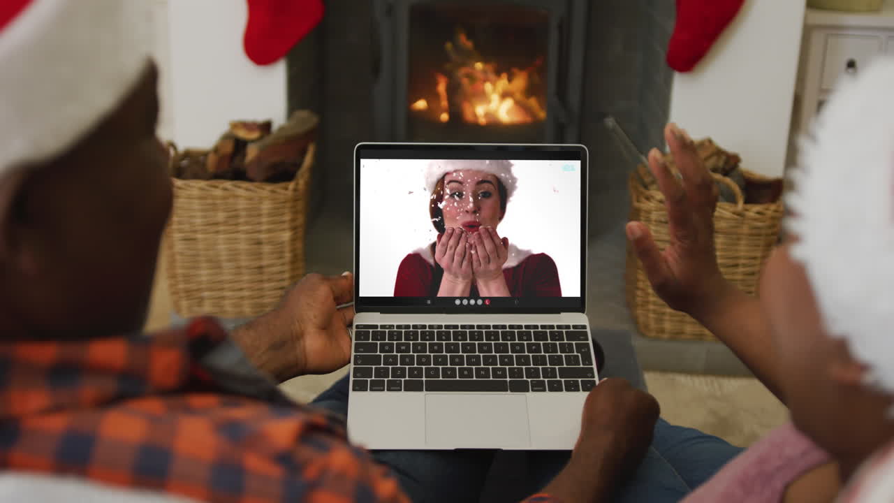 Coppia afroamericana con cappelli di Babbo Natale che usa un laptop per una videochiamata di Natale con una donna sullo schermo