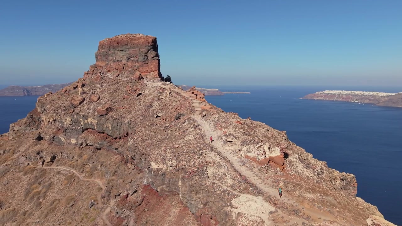 Drone kiertää Skaros-kalliota Santorinilla, paljastaen kallionrinteen polun ja portaat ja kuvaten dramaattista kalderamaisemaa Egeanmeren yläpuolella.