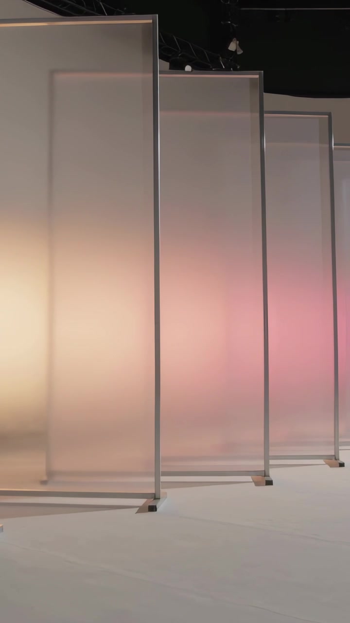 Video verticale: Telecamera che panoramica lungo una fila di pannelli satinati in studio, retroilluminazione che mostra una sfumatura rosa.