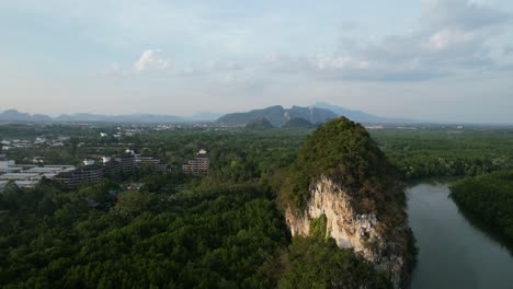 aerial-drone-panning-right-over-a-large-limestone-mountain-rocks-and-resort-in-the-distance-with-a-river-in-between-during-a-sunset-afternoon-in-Krabi-Town-Thailand