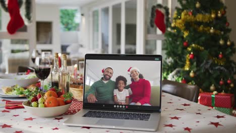 Glückliche-Afroamerikanische-Familie-Mit-Weihnachtsmützen-Auf-Laptop,-Der-Auf-Dem-Weihnachtstisch-Liegt
