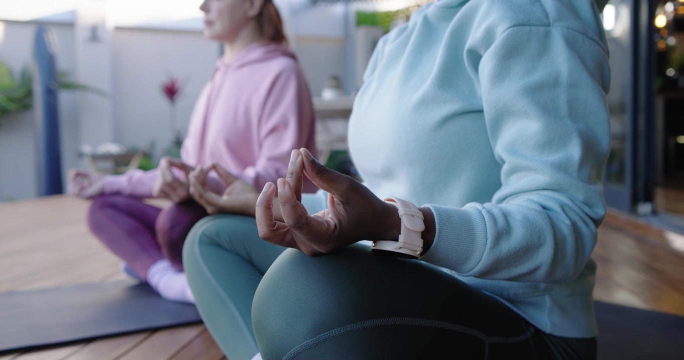Donne diverse più un'anziana che si sistemano su tappetini da balcone, alzando le mani in mudra per la calma, mostrando l'orologio