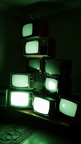 stack of vintage televisions with green glowing screens in a dark room
