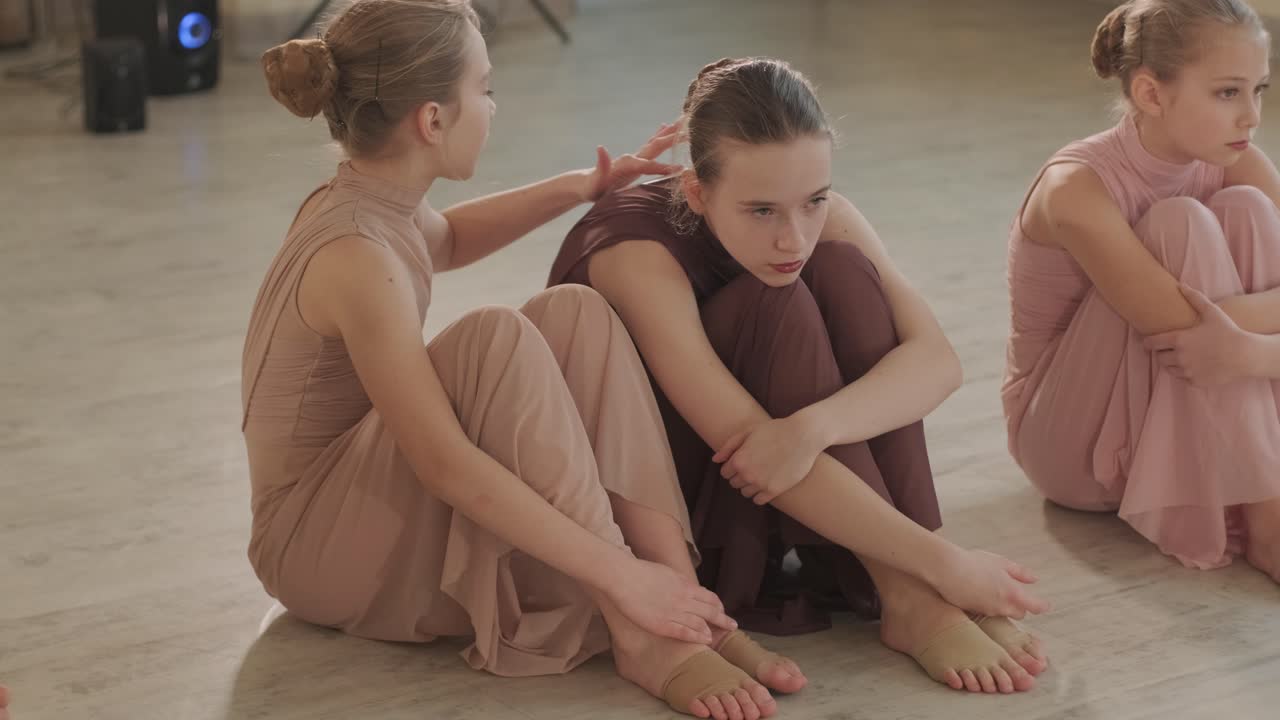 un grupo de jóvenes estudiantes de ballet con ropa de baile negra practicando posiciones en un amplio estudio de ballet con pisos de madera y barras montadas en la pared. expresiones enfocadas y movimientos sincronizados.