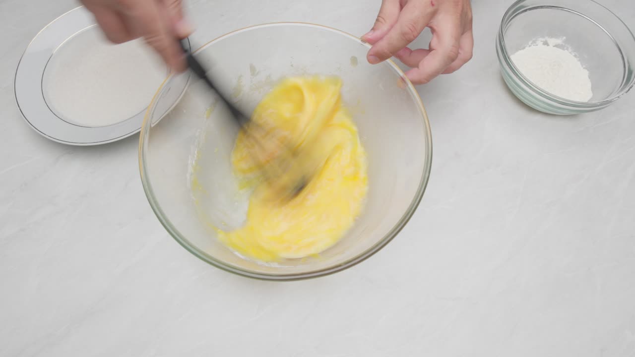 Hands whisking eggs in a glass bowl during cake preparation