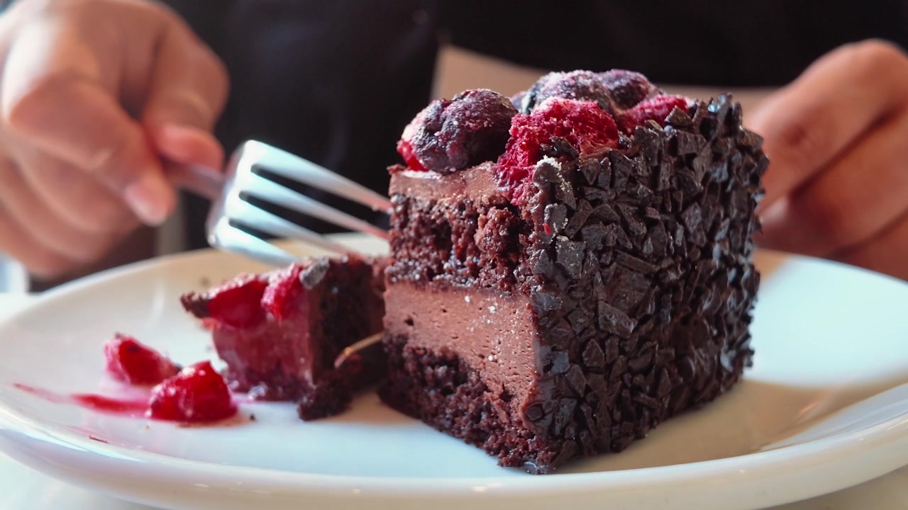 Persona che mangia una fetta di torta al cioccolato con frutti di bosco