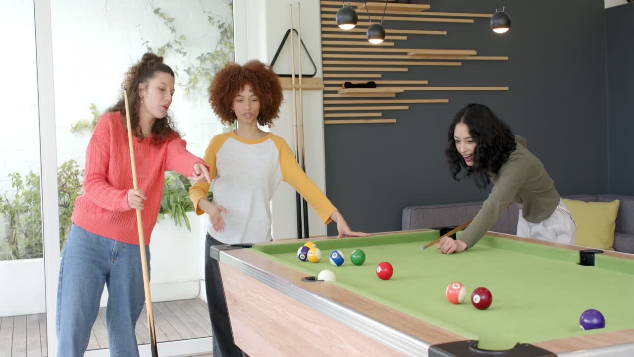 Amiche diverse che discutono di strategia al tavolo da biliardo, tirando la palla bianca per spaccare il triangolo, esultando