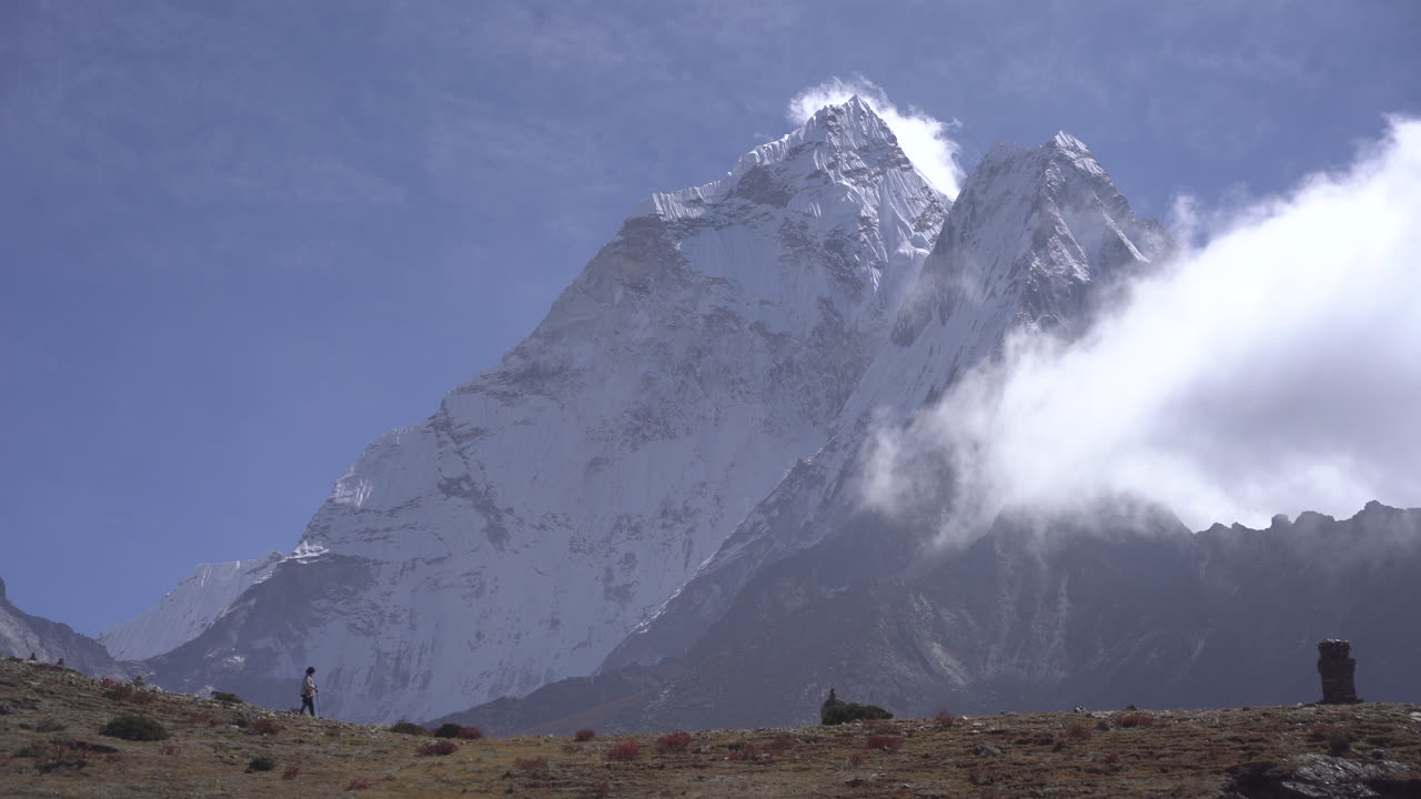 A tourist walking and exploring the Himalayan region of Everest Base Camp trek, with Ama Dablam towering in the background, clouds gently touching the snow-capped mountains in a lively environment