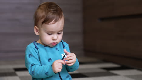 little cute baby focused on the cord in his hands. adorable caucasian toddler playing with a lace sitting on the floor indoors. blurred backdrop.
