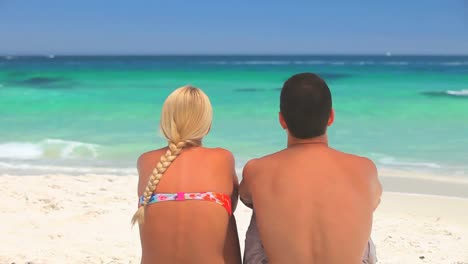 Young-man-sitting-on-a-beach-with-his-arm-around-his-girlfriend