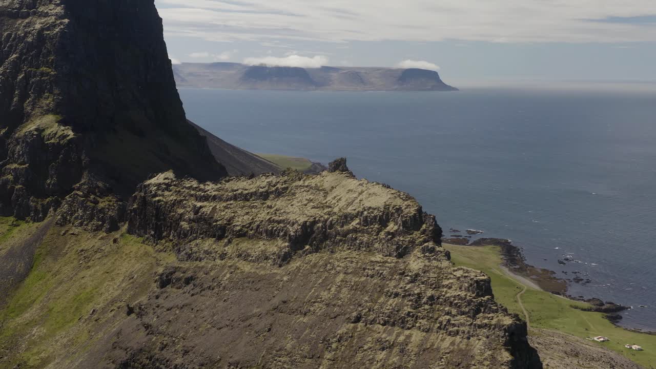un avión no tripulado gira alrededor de un pico más bajo en un acantilado de montaña rocosa en las costas occidentales de los fiordos de islandia