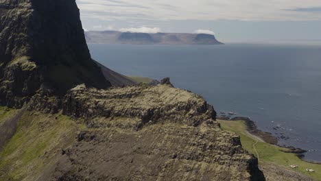 drone shot rotating around a lower peak on a steak rocky mountain cliff on the western fjord shores of iceland