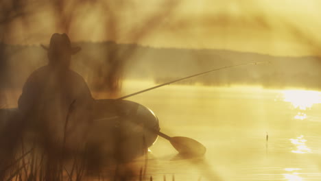 rear view of an old man with a hat on a boat fishing with a rod on the lake on a cloudy morning