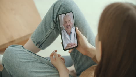 female medical assistant wears white coat headset video calling distant patient on smartphone. doctor talking to client using virtual chat telephone app. telemedicine remote healthcare services