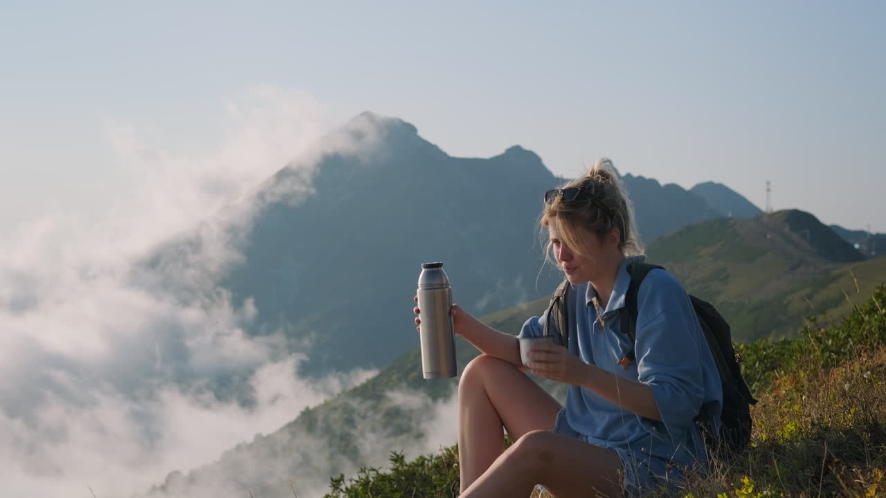 mujer disfrutando de una bebida en la cima de una montaña con vistas a las nubes