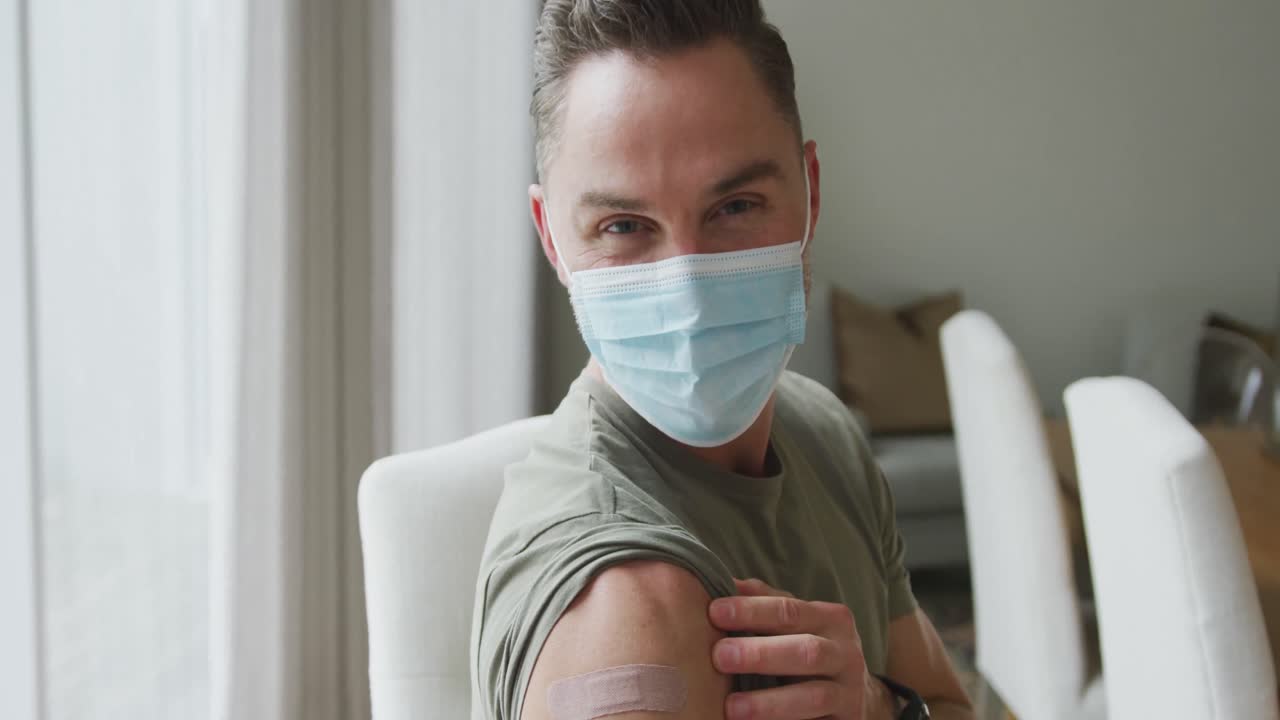 Ritratto di uomo caucasico con mascherina che mostra la spalla vaccinata a casa.