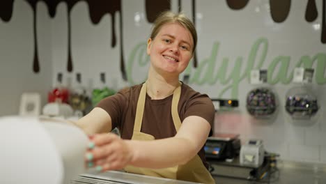 Portrait-of-a-confident-and-happy-girl-worker-in-the-confectionery-department-smiling-and-posing-in-a-brown-T-shirt-and-apron-in-a-supermarket