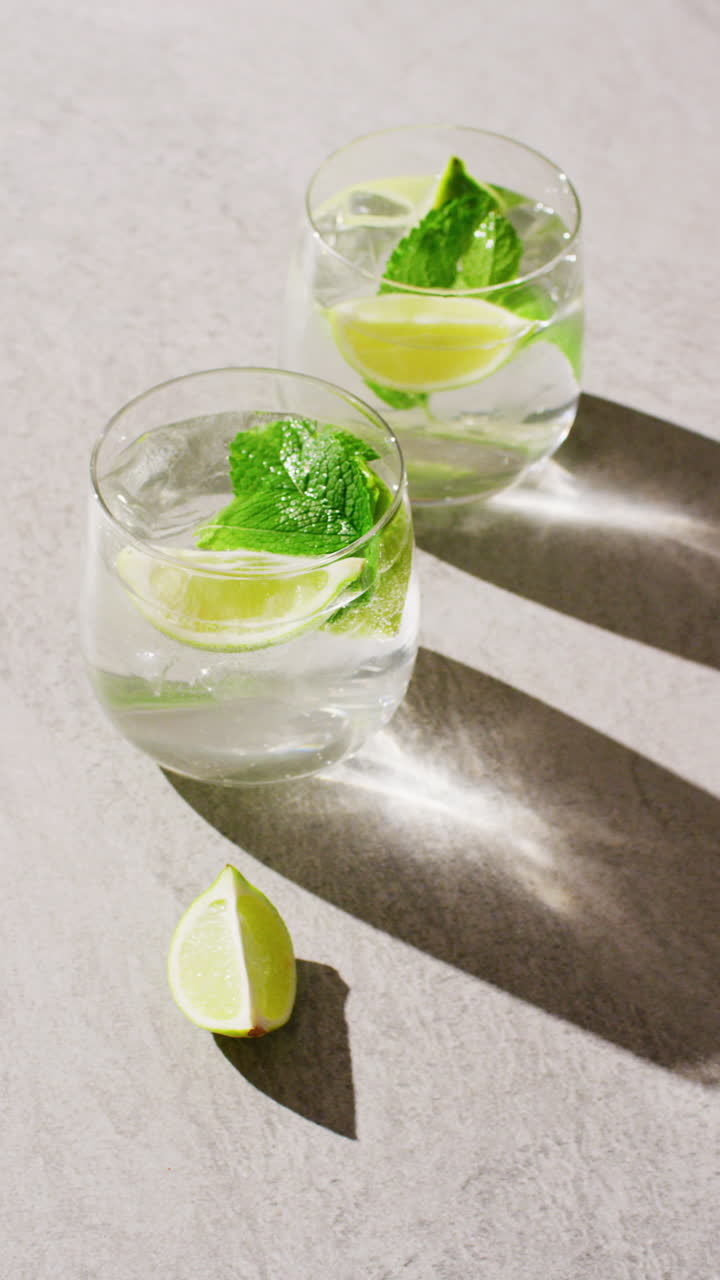 Vertical video of close up of drinks with lemons on white background