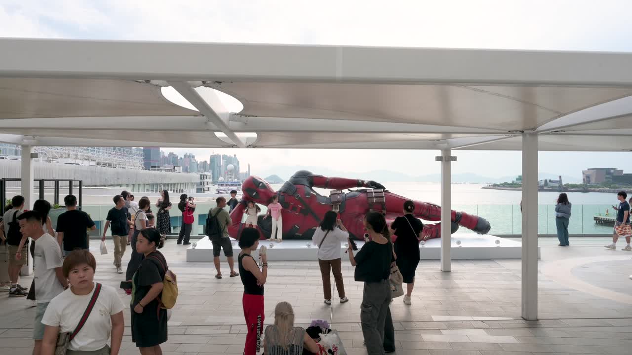 Locals and tourists visit the 8-meter Deadpool statue in Hong Kong, set up to promote Disney’s "Deadpool and Wolverine" movie, as the city skyline stands tall behind it.