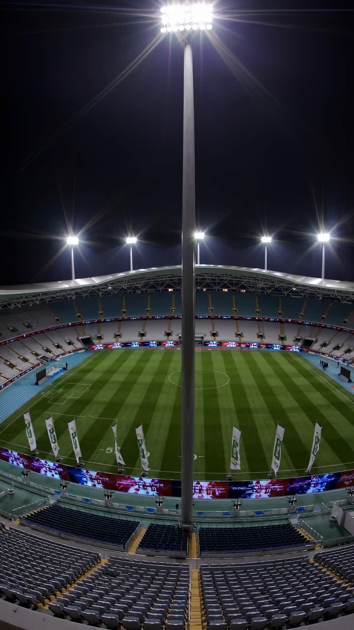 Ripresa video grandangolare di uno stadio illuminato a giorno di notte, che mostra i sedili vuoti e il campo verde.