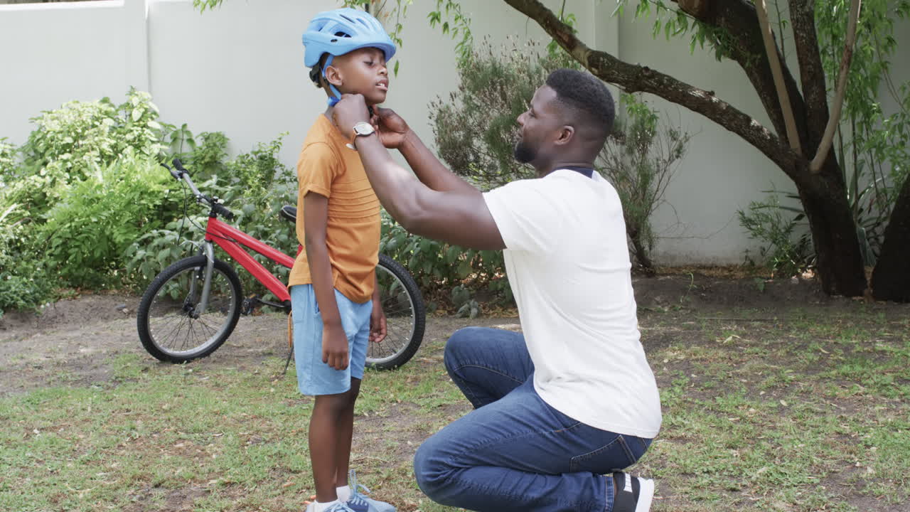 African American father helps a son with his helmet outdoors