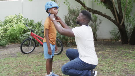 african american father helps a son with his helmet outdoors