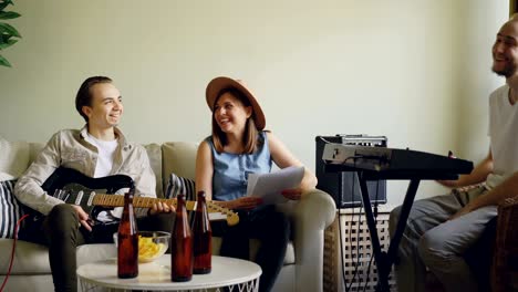 amigos alegres músicos están hablando discutiendo música durante el ensayo en casa. el tecladista está practicando mientras el vocalista y el guitarrista están escuchando y hablando.