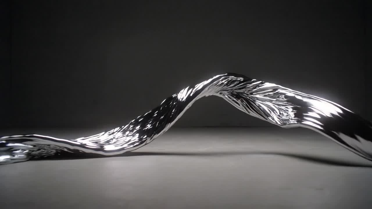 Reacting to hidden motor pulse, metallic ribbon forming traveling loop on studio floor, with lights