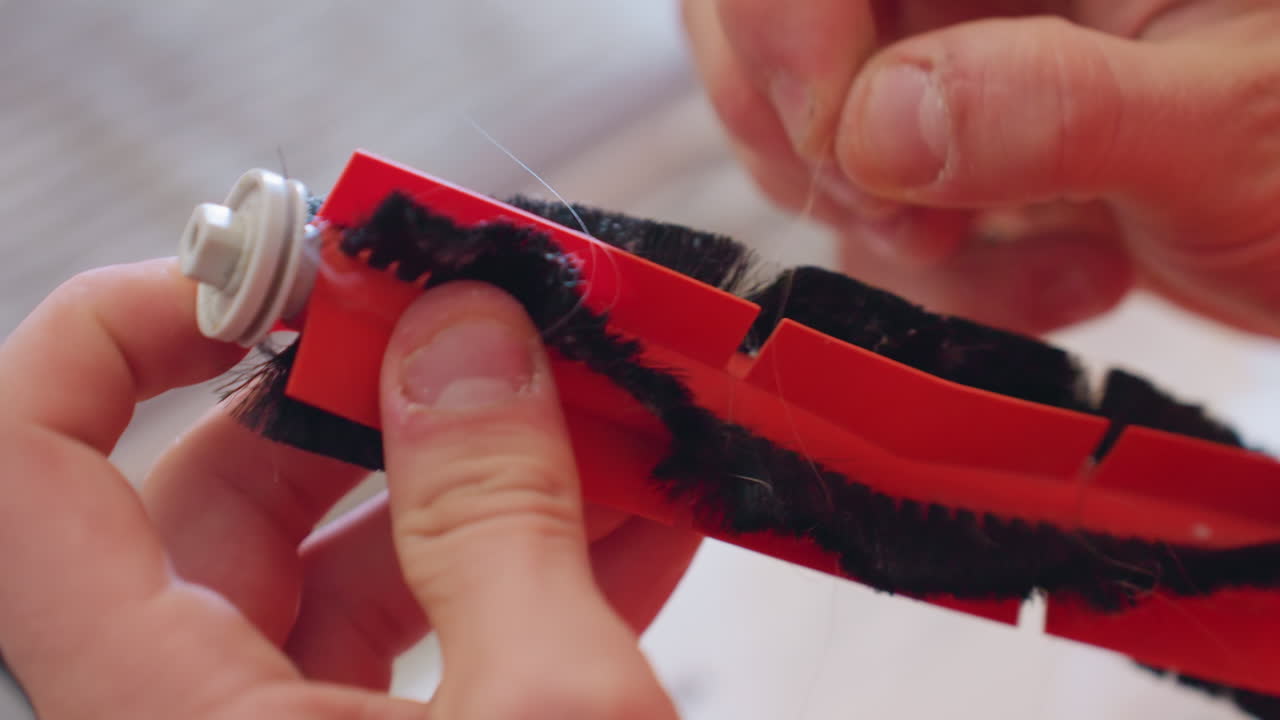 Close up of hands carefully removing tangled hair from vacuum cleaner rotating brush to ensure smooth performance, maintenance, and efficient cleaning of household appliance during repair process