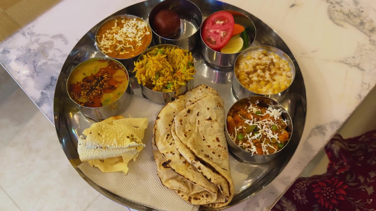 Orbiting shot of a traditional Indian vegetarian thali featuring assorted curries flatbread rice dessert and accompaniments served on a stainless steel platter