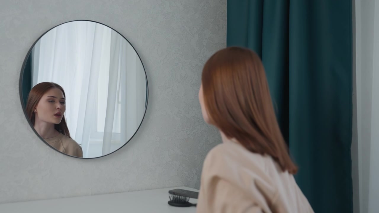 Studente caucasico che controlla il riflesso nello specchio in camera da letto con tende color verde acqua, studia postura ed espressione prima di una lezione online, si sistema i capelli e il maglione, atmosfera introspettiva con luce soffusa