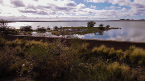 Drone-dolly-riser-over-Beaufort-West-dam-wall-and-surface-with-beautiful-sky