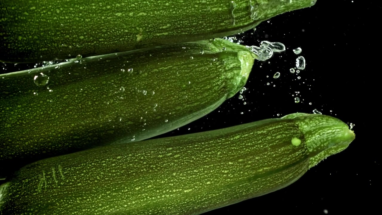 Zucchine verdi fresche che cadono nell'acqua al rallentatore.